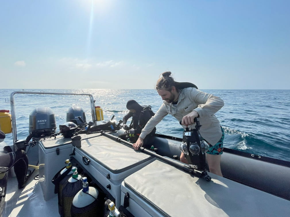 A field team prepares a custom underwater 360° camera rig on a research vessel before deploying it at sea.