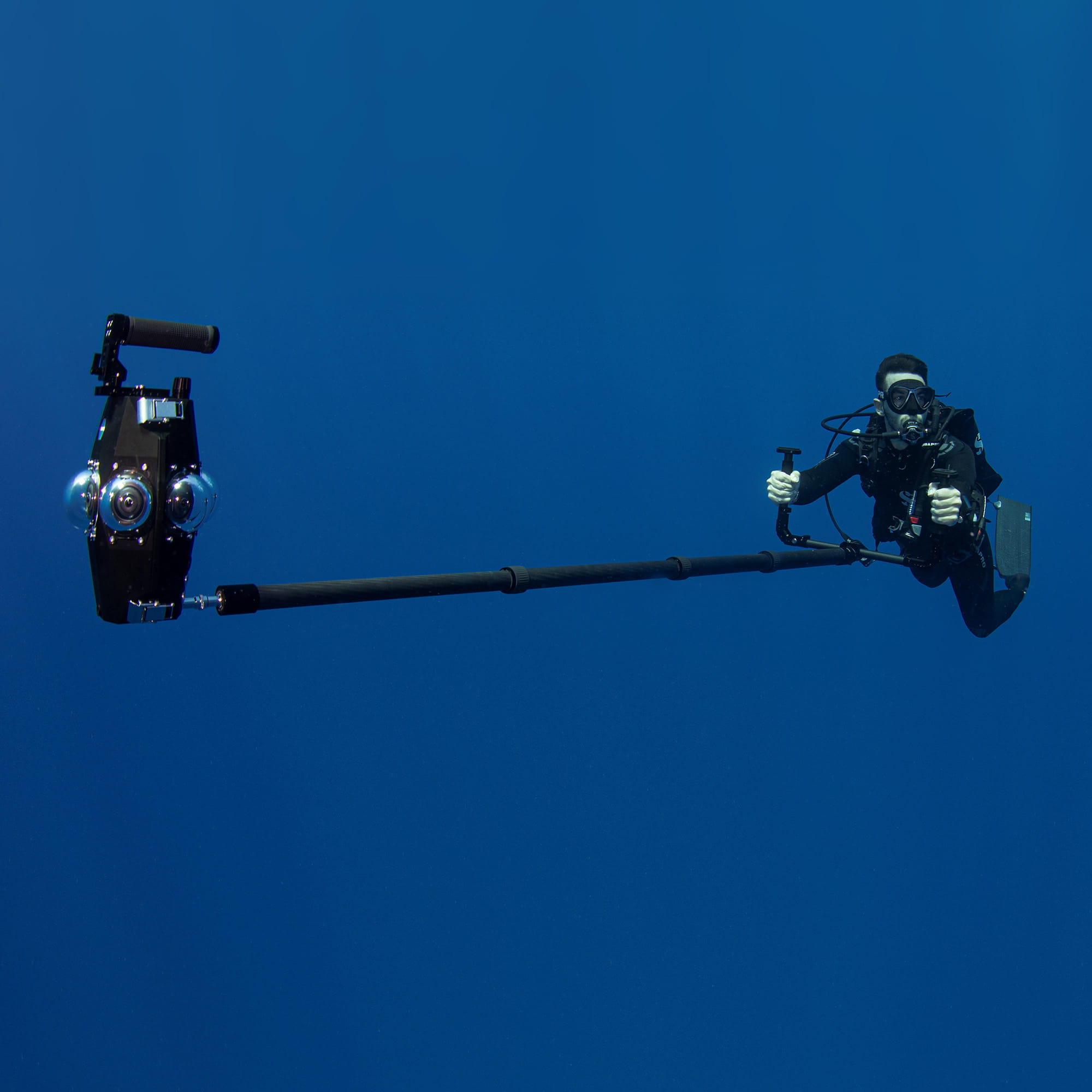 A diver operates a custom underwater 360° camera rig on an extended pole, capturing immersive footage in open ocean conditions.